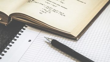 Plano aproximado de uma caneta e de um livro de matemática sobre um caderno quadriculado